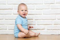 Малыш смотрит в камеру и сидит на фоне белой кирпичной стены. — стоковое фото