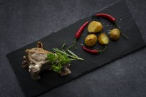 Roast lamb with potatoes on slate garnished with parsley and chillies — Stock Photo