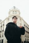 Handsome young man in black hooded jacket standing on city street — Stock Photo