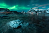 Capa de hielo agrietada en el agua con montañas bajo luces del norte por la noche - foto de stock