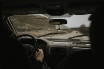 Vista posteriore della persona irriconoscibile che guida un'auto moderna lungo la strada di campagna nella giornata grigia — Foto stock