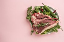Rohes Rindersteak auf Teller mit Zutaten auf rosa Hintergrund — Stockfoto