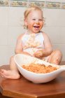 Весела маленька дитина сидить на казці і розважається під час їжі макаронних виробів з миски . — стокове фото