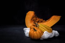 Fresh whole pumpkins with piece on white cloth on black background — Stock Photo
