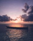 Bateau vide flottant dans l'océan sous le ciel nuageux et le coucher du soleil. — Photo de stock