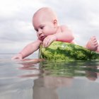 Веселий оголений малюк сидить у кавуні на воді — стокове фото