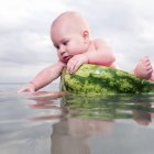 Cheerful nude toddler boy sitting in watermelon on water — Stock Photo