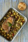 Roast lamb with potatoes in backing dish on shabby wooden table with bread — Stock Photo