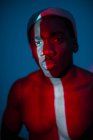 Етнічний чоловік без емоцій стоїть зі світловою лінією на тілі і дивиться на камеру — стокове фото