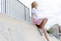 Stylish blonde girl in sunglasses sitting in skate park — Stock Photo