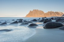 Smooth dark stones in long exposure flow of water on background of cliffs, Lofoten, Norway — Stock Photo