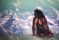 Junge Frau im Badeanzug sitzt im Studio vor dem Hintergrund des Meeres — Stockfoto