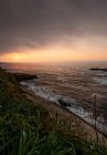 Mar tempestuoso salpicando perto da encosta gramada ao pôr do sol à noite nublado, Astúrias, Espanha — Fotografia de Stock