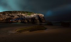 Silhouette di persona anonima con torcia luminosa in piedi sulla costa vicino al mare e scogliera nella notte nuvolosa, Asturie, Spagna — Foto stock