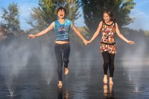 Азиатки прыгают на фонтанной воде — стоковое фото