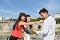 Азиатские женщины улыбаются и чистят свитер мужчины, стоя рядом с фонтаном парка вместе — стоковое фото