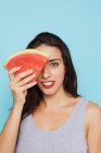 Giovane donna che copre l'occhio con pezzo di anguria su sfondo blu — Foto stock