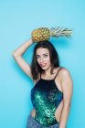 Молодая женщина позирует в блестках праздничный топ позируя с ананасом на синем фоне — стоковое фото