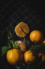Fresh ripe tangerines with green leaves on black background — Stock Photo