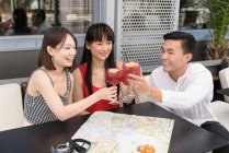 Троє азіатців посміхаються і чіпляються за склянки смачного напою, сидячи за столом біля карти. — стокове фото