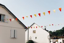 Bandeiras triangulares coloridas penduradas entre encantadoras casas suburbanas contra o céu azul claro — Fotografia de Stock