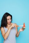 Young woman in bodysuit cutting watermelon with knife on blue background — Stock Photo