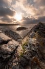 Picturesque view of cloudy sky with bright rising sun over calm sea and rough boulders, Asturias, Spain — Stock Photo
