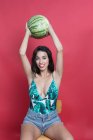 Young woman in denim shorts and top holding watermelon above head — Stock Photo