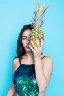 Jovem mulher em brilho top cobrindo olho com abacaxi no fundo azul — Fotografia de Stock