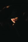 Приваблива молода жінка, що покриває половину обличчя капелюхом, стоячи в темній кімнаті — стокове фото