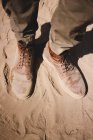 Piernas de viajero en botas sucias de pie sobre arena - foto de stock