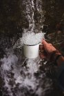 Hand des Menschen hält Becher unter Süßwasser kaltem Wasser Quelle in der Natur — Stockfoto