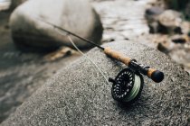 Close-up of fishing rod on smooth boulder on shore in nature — Stock Photo