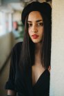 Приваблива молода жінка в чорному береті дивиться на камеру, спираючись на стіну вдома — стокове фото