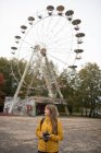 Rückansicht einer blonden Frau mit Kamera, die ein Foto von einem verlassenen Freizeitpark mit Attraktionen macht — Stockfoto
