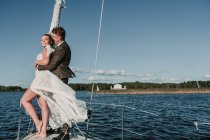 Seitenansicht eines glücklichen Ehepaares, das auf der Nase der Jacht steht und sich am See umarmt — Stockfoto