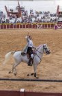 España, Tomelloso - 28. 08. 2018. Vista de la mujer torero cabalgando en la zona arenosa con la gente en tribuna - foto de stock