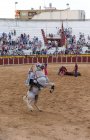 Spanien, Tomelloso - 28. 08. 2018. Ansicht einer Stierkämpferin, die auf einem Pferd reitet und mit einem Stier auf sandigem Gelände kämpft, mit Menschen auf der Tribüne — Stockfoto