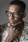 Portrait of serious African American man in golden accessories and glasses touching chin — Stock Photo
