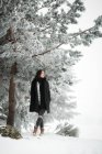 Hübsche junge Frau in stylischem Outfit schaut weg, während sie an kalten Tagen in einer wunderschönen Landschaft neben einem schneebedeckten Baum steht — Stockfoto