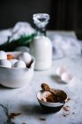 Tigela e colher de cacau em pó em pé sobre mesa de mármore perto de tigela de ovos frescos e garrafa de leite agradável — Fotografia de Stock