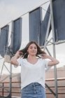 Очаровательная молодая женщина в белой рубашке и джинсовой юбке гладит волосы стоя на городском фоне — стоковое фото