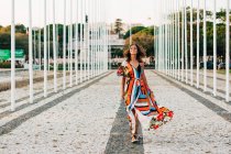 Conteúdo mulher em vestido ornamental colorido andando em calçada calçada sorrindo para a câmera — Fotografia de Stock