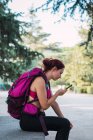 Спортсменка с рюкзаком просматривает смартфон в парке — стоковое фото