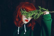 Jeune femme rousse couvrant les yeux avec une brindille de sapin vert sur fond noir — Photo de stock