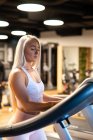Jeune femme blonde jogging sur tapis roulant dans la salle de gym — Photo de stock