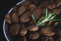 Dried almonds in bowl with rosemary sprig — Stock Photo