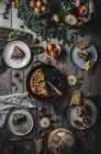 De dessus vue de tortilla fraîche savoureuse sur la casserole près des assiettes avec des tranches, tomates, fruits, noix et feuilles sur panneau de bois — Photo de stock