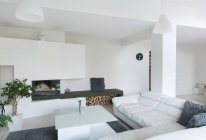 Sala de estar moderna feita em cor branca mobilada com sofá de couro acolhedor e mesa com lâmpadas penduradas no teto — Fotografia de Stock