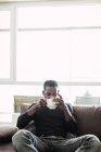 Pensive black man relaxing on sofa with coffee — Stock Photo